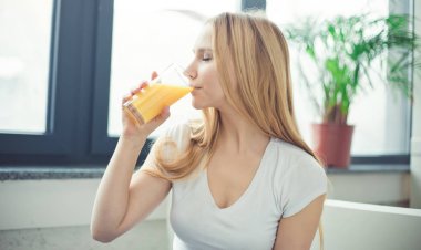 Gülümseyen güzel genç sarışın kadın evde kanepede oturan bir bardak taze portakal ile.