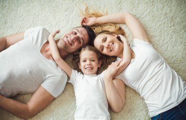 Üstten Görünüm genç mutlu aile. Güzel ve annem ve babam evde yerde yatarken ve kameraya bakarak sarılma kızı ile gülümseyen.