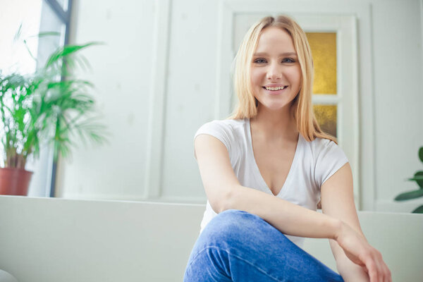 Портрет красивой улыбающейся молодой блондинки, сидящей дома на диване и отдыхающей или расслабляющей
.