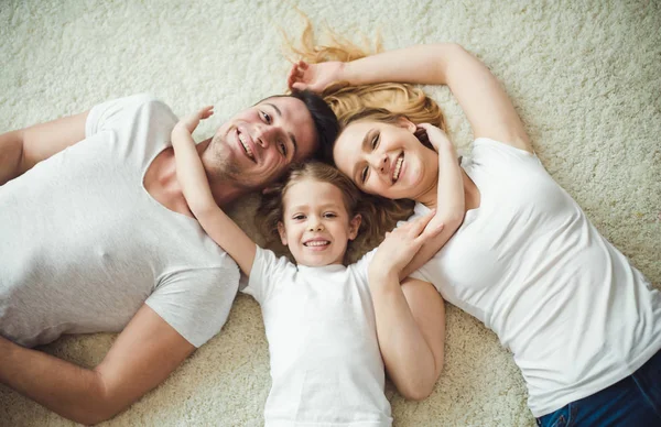 年轻幸福家庭的最高视图 美丽和微笑的父亲和母亲与女儿躺在地板上在家和拥抱看着相机 — 图库照片