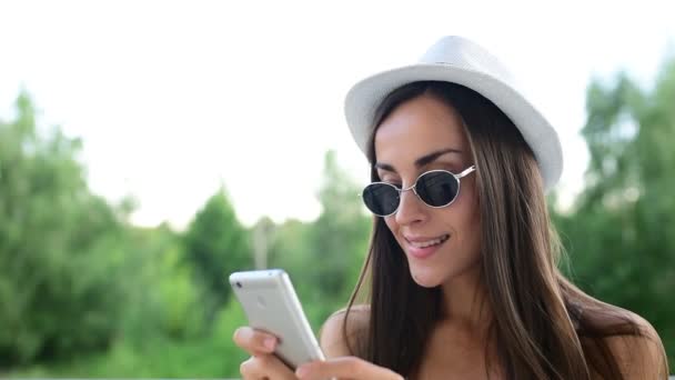女人给男朋友写信息 年轻开朗迷人的帽子和太阳镜女孩使用电话 并在它玩游戏 — 图库视频影像