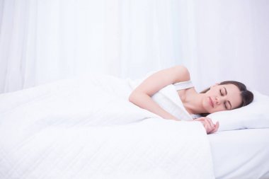 Genç güzel gülümseyen kadın tatlı bir şekilde evde beyaz bir yatakta uyuyor. Rahatlamak ve dinlenmek.