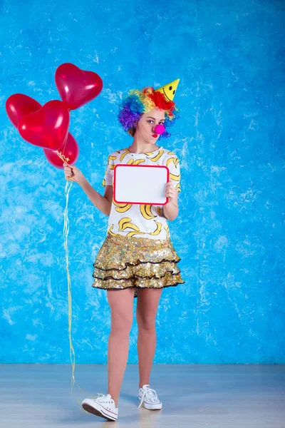 Happy clown. Concept of holidays. A cheerful young girl in a clown suit posing in front of a camera on a blue background. 1 April Fools' Day concept. Birthday.