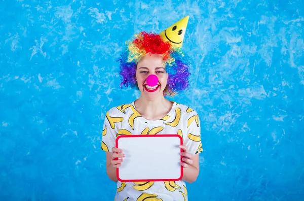 Happy clown. Concept of holidays. A cheerful young girl in a clown suit posing in front of a camera on a blue background. 1 April Fools' Day concept. Birthday.