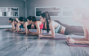 Mutlu grup genç güzel kadınların tahta konumda yoga egzersizleri yapıyor spor giyim. Açık veya yoga sınıfı