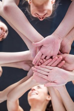 Close up photo of young smiling women putting their hands together. Friends with stack of hands showing unity and teamwork.