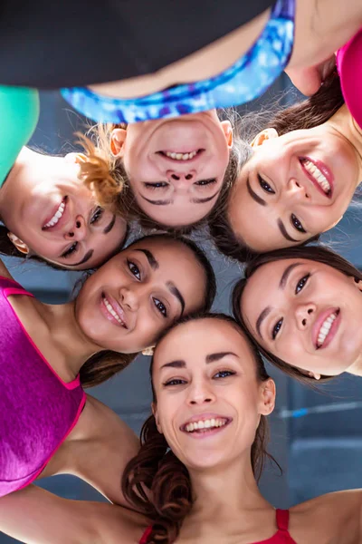 Sports friendship. Six beautiful smiling sportive women lie head to head on the floor in the gym and have fun looking at the camera