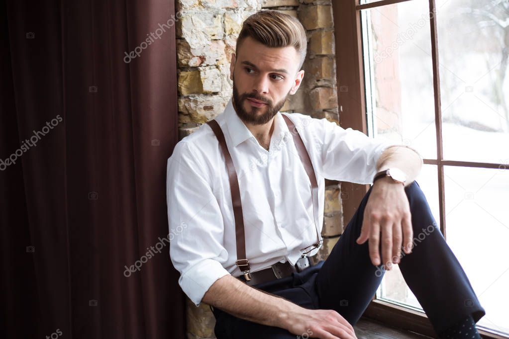 Fashion stylish confident portrair of handsome bearded guy on the big window looking away