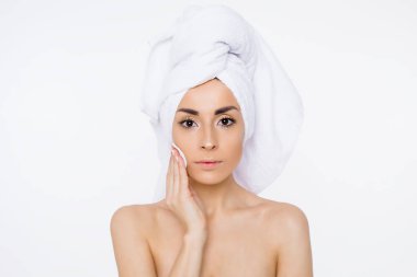 Kaldırma makyaj. Güzellik ve spa. Kafasındaki bir havlu ile güzel bir gülümseyen kadın nemlendirir veya pamuklu ped kullanarak makyaj yüzünü temizler. Kozmetik. Kadın sağlığı