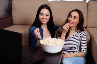 İki çekici kız arkadaşlar evde Tv ya da film izlerken ve patlamış mısır yemek.