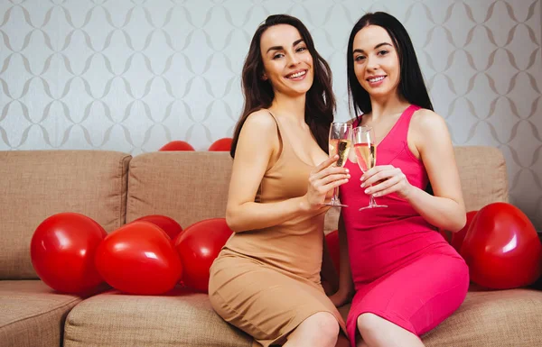 母鸡党 两个美丽开朗的女孩朋友在明亮的晚礼服喝香槟和休息在一个聚会上坐在沙发上 — 图库照片