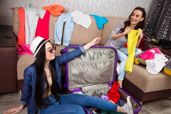 We are ready to go to rest at sea. Two beautiful cheerful women fold clothes for a trip to suitcases.