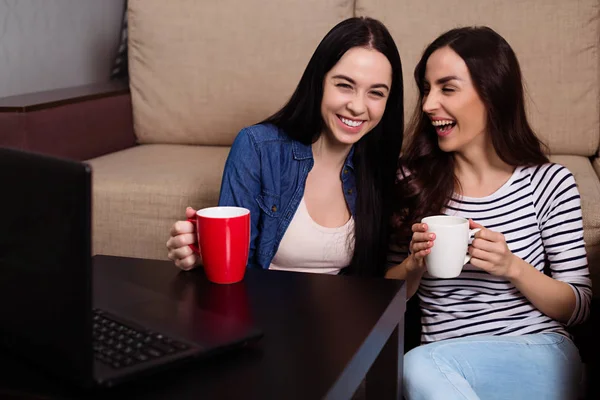 コーヒーでラップトップで映画を見たり 自宅のソファでお茶 つの美しい笑顔の姉妹 — ストック写真
