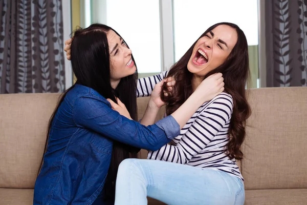 Two aggressive young women fight and wrest one another\'s hair.