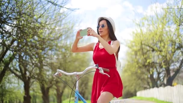 愉快和愉快的美丽的年轻女孩使用电话与复古自行车在城市公园 — 图库视频影像