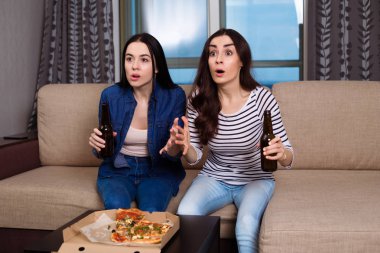 Modern kız arkadaş kanepede oturan rahat kıyafetler içinde gülümseyen güzel iki vejetaryen pizza yemek ve kameraya bak.