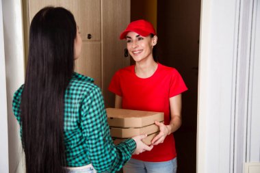 Daire ya da ev müşteriye pizza üç kutu kırmızı üniformalı genç gülümseyen kız kurye teslim.