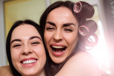 Güzel gülümseyen genç kız bir parti için hazırlanıyor ve kanepede oturan saç yapıyor