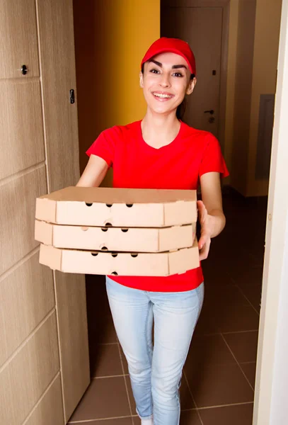 Service delivery of food at home. A young smiling girl courier in red uniform delivered  pizza in apartment