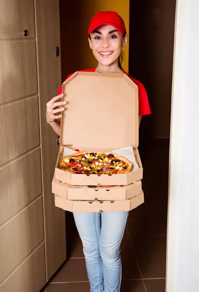 Service delivery of food at home. A young smiling girl courier in red uniform delivered  pizza in apartment