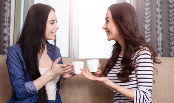 两个微笑的美丽的妇女喝咖啡或茶在家里和讨论新闻 — 图库照片