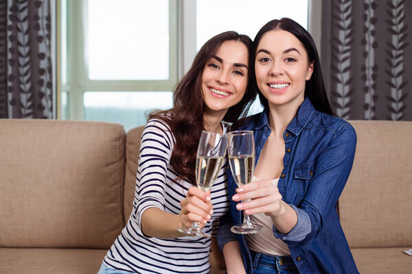 Улыбающиеся красивые девушки в повседневной одежде разговаривают и пьют шампанское дома на диване
.