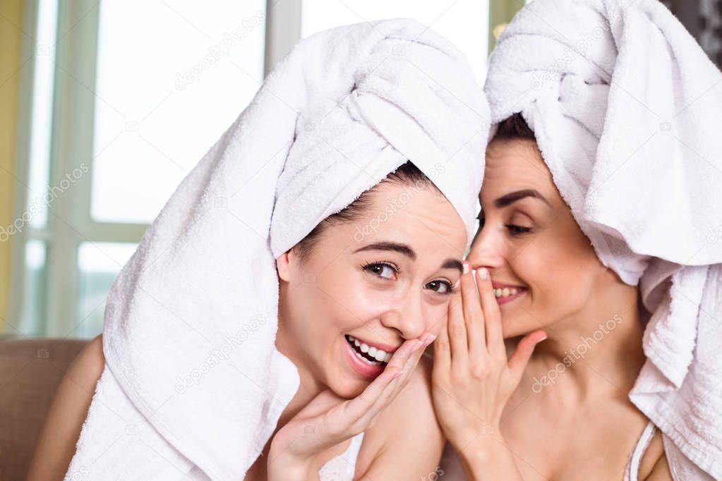 Beautiful smiling young  friends in white towels on their heads after a spa gossip or discuss something sitting on the couch. The girls are resting.