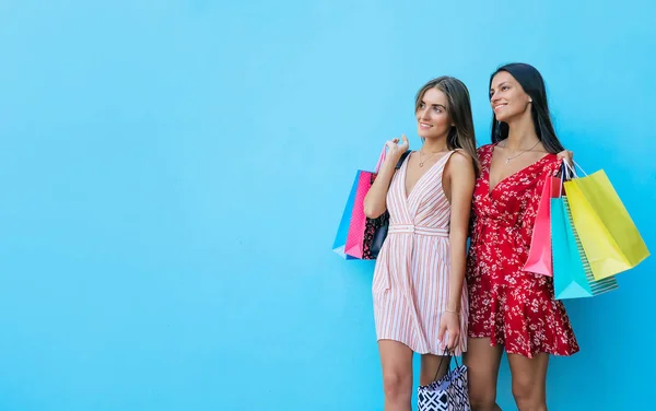 ショッピングコンセプト 買い物中の女の子の友人 青い背景にショッピングバッグを持つ2つの陽気な美しい笑顔の女性 — ストック写真