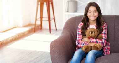 Kanepede oturan ve oyuncak ayıyı tutan genç kız. 