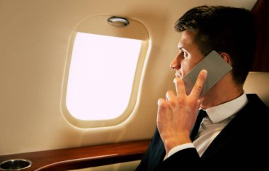 Uçaktaki genç işadamı akıllı telefondan konuşuyor. 