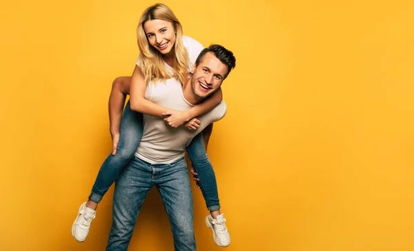 happy couple on studio background. man giving piggyback ride to woman