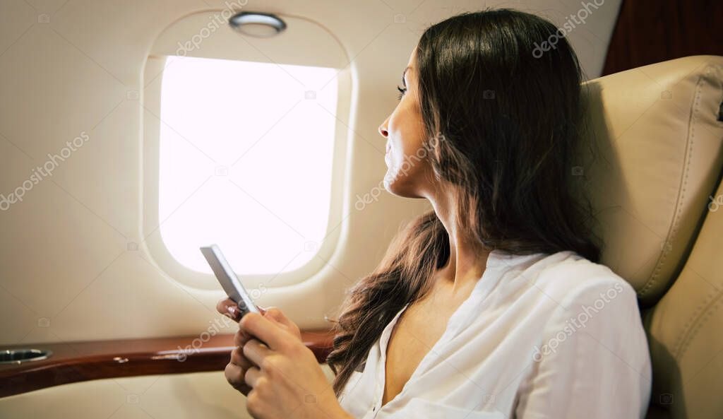 Young woman on plane holding smartphone 