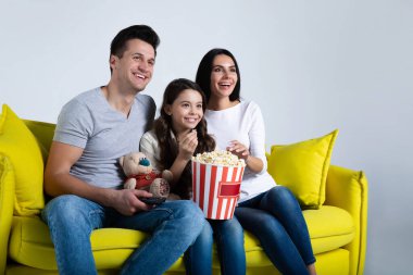 Evde patlamış mısırla televizyon izleyen mutlu bir aile. Sarı koltukta oturuyor.