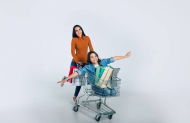 Beyaz arka planda alışveriş arabası olan mutlu anne ve kız ailesi.