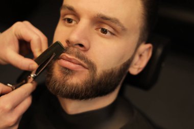 Genç bir adamın tımarı. Berber dükkanında sandalyede otururken sakallı bir adam kuaförde sakal tıraşı oluyor.