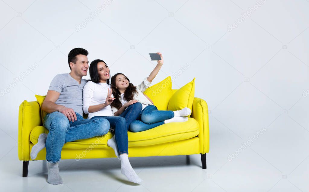 portrait of happy young family sitting on yellow sofa taking selfie