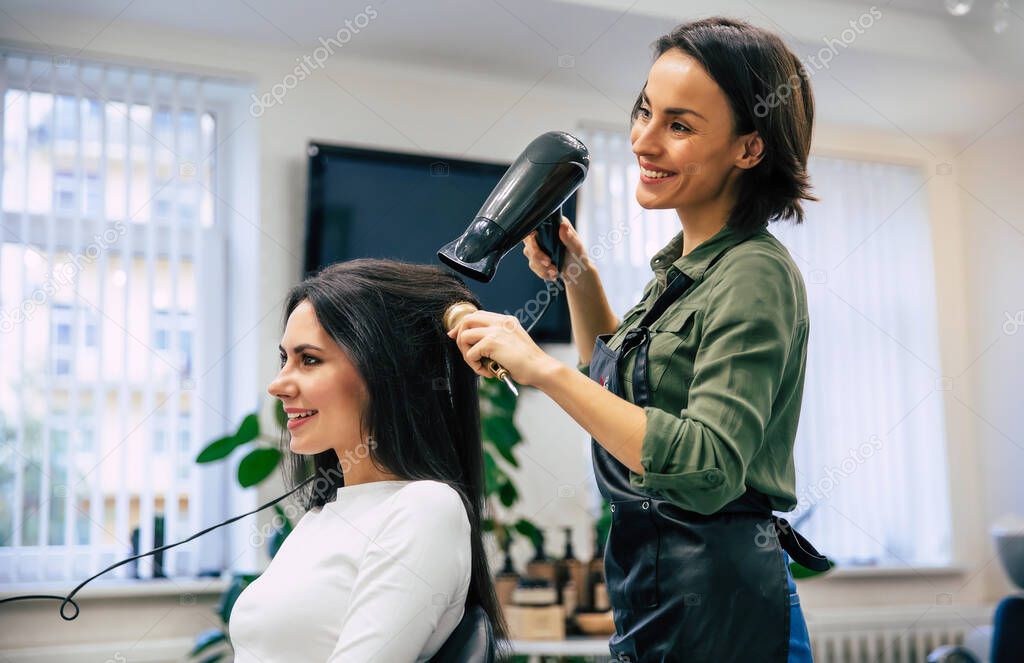 Female hairdresser smiling, making hairstyle to young woman in beauty salon