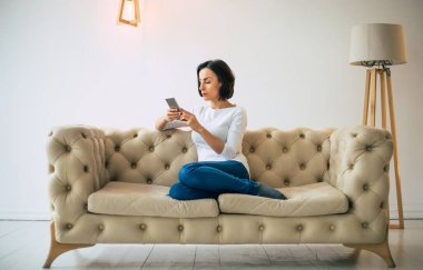 Google araması. Gündelik kıyafetli genç bir kız modern dairesinde rahat bir koltukta oturuyor ve elindeki akıllı telefonun ekranına bakıyor..