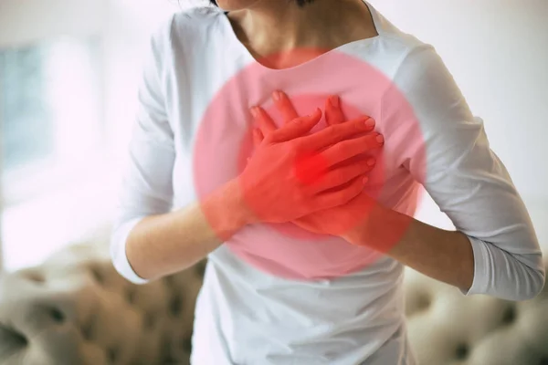 Heart attack. Close-up photo of woman\'s hands touching her heart area highlighted in red, while she is suffering from chest pain.