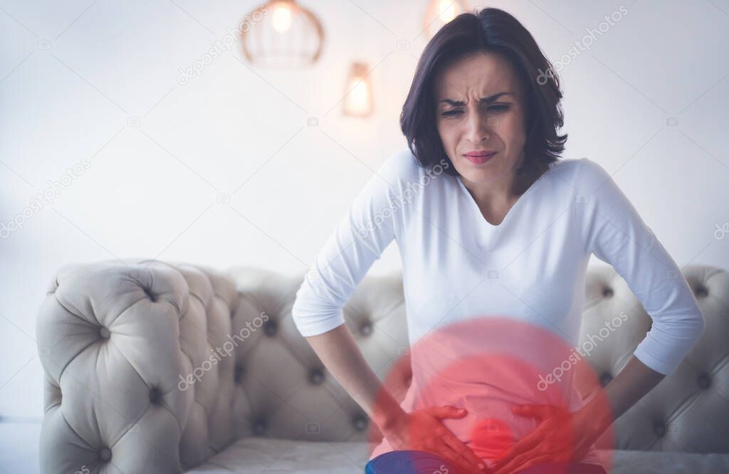 Intense ache. Close-up photo of a young woman touching her lower stomach area, which is highlighted in red.