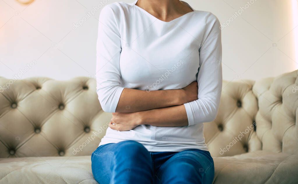 Stomachache. Close-up profile photo of a woman holding her belly while sitting on a couch.