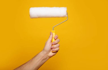 Boya merdiveni. Sarı arka planda resim rulosu tutan bir elin yakın plan fotoğrafı. Ev yenileme konsepti.