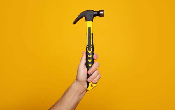 Carpenter hammer. Close-up photo of a hand holding a hammer on a yellow background. Home renovation concept.