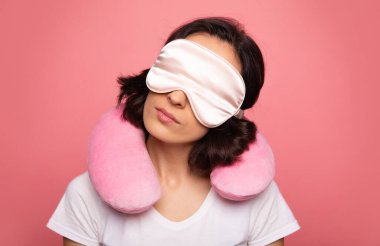 Uyumaya hazır. Gözlerine maske takan ve omuzlarına boyun yastığı takan genç bir kadının yakın plan fotoğrafı..