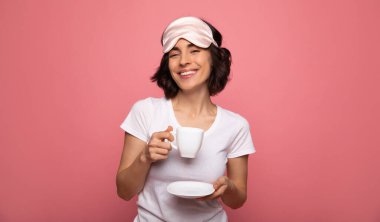 Sabah rutini. Yüzüne maske takmış, gülümseyen ve sıcak kahvesini yudumlayan mutlu genç bir kızın yakın plan fotoğrafı..
