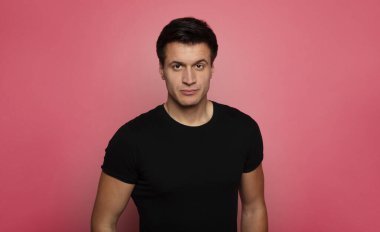 Erkeklik. Siyah tişörtlü, kameraya özgüvenle bakan ciddi bir gencin yakın plan fotoğrafı..