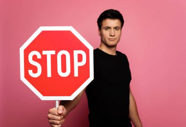 Güçlü ol! Elinde dur tabelası tutarken kameraya bakan, günlük kıyafetli ciddi bir adamın yakın plan fotoğrafı..