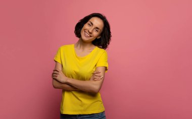 Gülen surat. Sarı elbiseli çekici bir genç kadının yakın plan fotoğrafı. Kameraya büyük bir gülümsemeyle bakıyor ve kollarını kavuşturmuş duruyor.. 