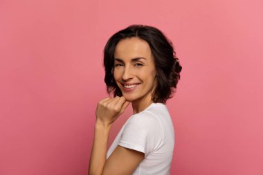 Cilveli. Kameraya bakıp çenesine dokunurken gülümseyen, gündelik elbiseli çekici bir kadının yakın plan fotoğrafı..