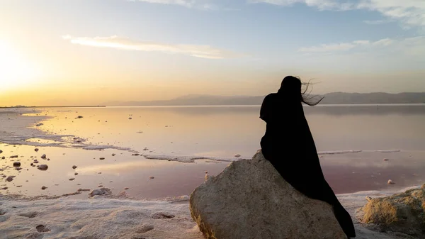 Azonosítatlan iráni nő hidzsáb burkában ül egy sziklán a Maharloo rózsaszín tó mellett, Shiraz, Irán — Stock Fotó
